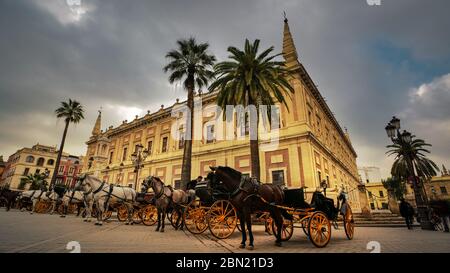 Seville, Spain - February 7th, 2020 - Parked horse-drawn carriages in front of the General Archive of the Indies (The Archivo General de Indias) in Se Stock Photo