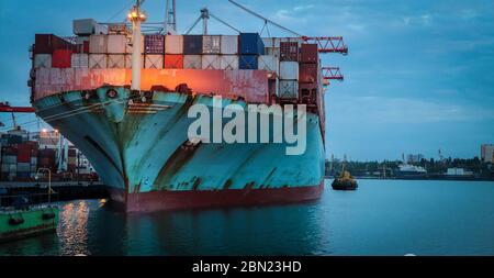 Container cargo ship load in the seaport at dusk. Logistics and transportation of Container Cargo ship with working crane bridge in shipyard, logistic Stock Photo