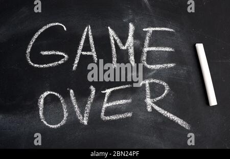 inscription in English game over with white chalk on a black board, concept of ending the process Stock Photo