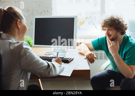 Young man sitting in office during the job interview with female employee, boss or HR-manager, talking, thinking, looks confident. Concept of work, getting job, business, finance, communication. Stock Photo