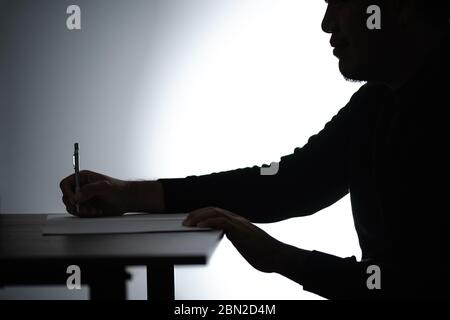 Silhouette asian man writing on table. Beared man writing on Notebook. Freelancer man Blogger writing at Home on desk. Stock Photo