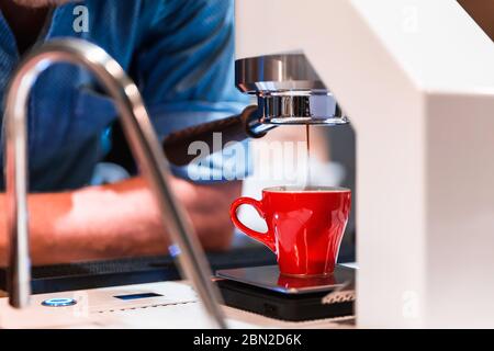 Barista waiting for coffee machine making an Espresso shot pouring out into the small red cup. Stock Photo