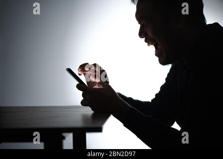 Silhouette asian man Working on smartphone. Beared man Works from home on cellphone. Freelancer man Blogger Working remotely at Home With mobile phone Stock Photo