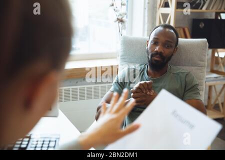 Young man sitting in office during the job interview with female employee, boss or HR-manager, talking, thinking, looks confident. Concept of work, getting job, business, finance, communication. Stock Photo
