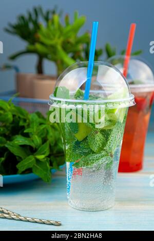 Mojito and Lemonade summer cold drink in a plastic glass with a straw. Coctail with mint, lemon, lime and ice. Serve at the bar. Beverage closeup. Stock Photo