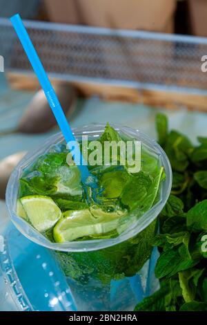 Mojito and Lemonade summer cold drink in a plastic glass with a straw. Coctail with mint, lemon, lime and ice. Serve at the bar. Beverage closeup. Stock Photo