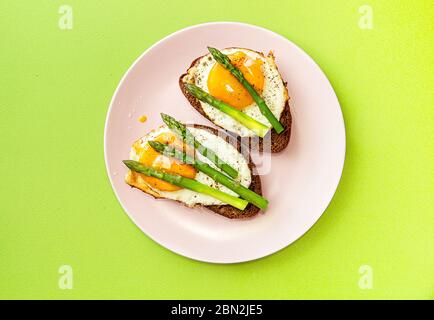 Delicious toast bread sandwiches with asparagus and fried eggs on pink plate over green background. top view, copy space Stock Photo