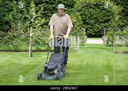 Man mowing a lawn in the grounds of a luxury home, lawncare and grass maintenance, UK Stock Photo