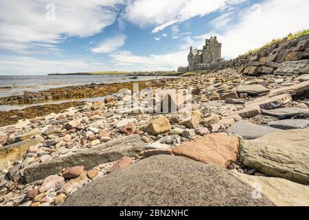 historic hotel of Ackergill Tower at Sinclair Bay in the Scottish Highlands. Rocky beach with the  beautiful and luxuary old british mansion in the ba Stock Photo