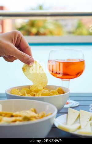 closeup of a young caucasian man taking a potato chip from a bowl placed on a table next to different other snacks and a glass with a red drink Stock Photo