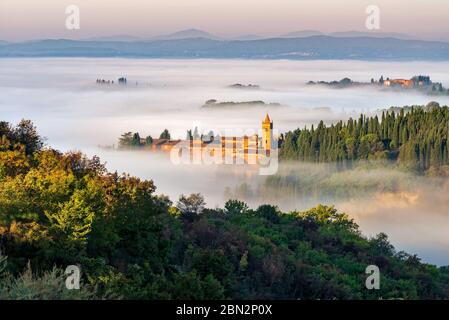 The abbey of Monte Oliveto Maggiore looks like an islands in an ocean of morning fog, crete senesi landscape, Siena, Italy
