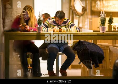 Young couple sits closely in a cafe staring at the one's phone Stock Photo