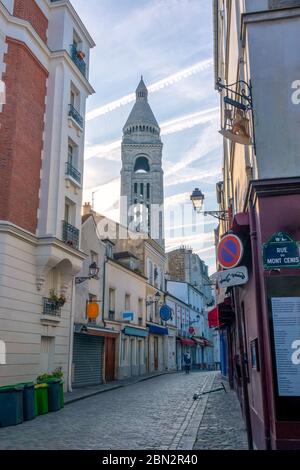 France. Sunny summer day in Paris. Narrow street with cobblestone pavement without cars. The old high bell tower Stock Photo