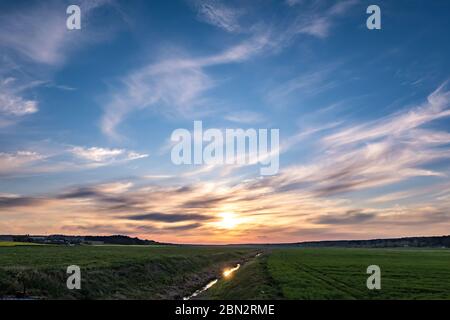landscape of green field with blue red pink evening sky with beautiful clouds after sunset Stock Photo