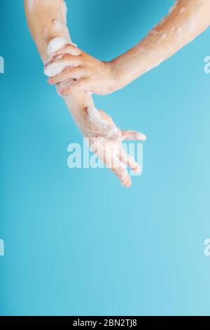 Hands of a child in soapy antibacterial foam, on a blue background, top view. Minimalistic concept of free space. Stock Photo