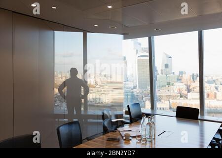 Silhouette businessman standing at urban highrise office window Stock Photo