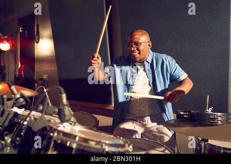 Smiling young male drummer playing drums in recording studio Stock Photo