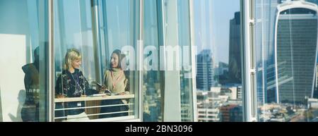 Businesswomen talking at sunny urban highrise office window Stock Photo