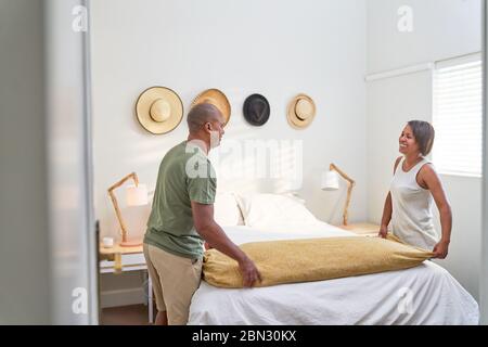 Couple making bed in bedroom Stock Photo