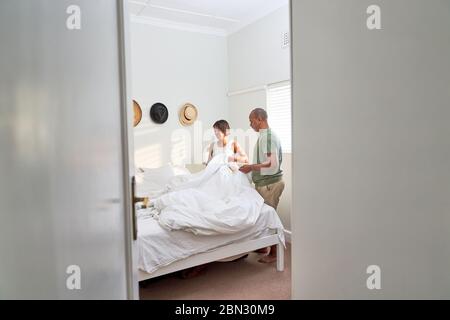 Couple making bed in bedroom Stock Photo