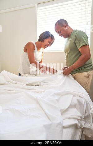 Couple making bed in bedroom Stock Photo