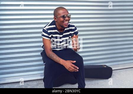 Happy male musician sitting on guitar case outside garage Stock Photo