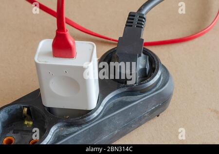 Old black extension cord on the floor with connected consumers. Extension cord with attached charger for smartphone and black electric plug. Electrica Stock Photo