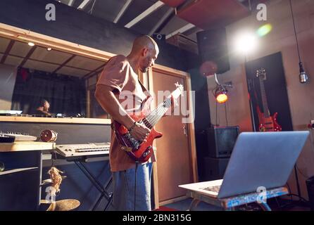Male musician practicing guitar at laptop in recording studio