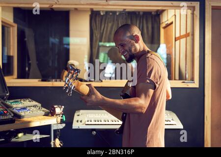 Happy male musician playing guitar in recording studio Stock Photo