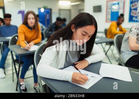 Focused high school girl student taking exam at desk in classroom Stock Photo