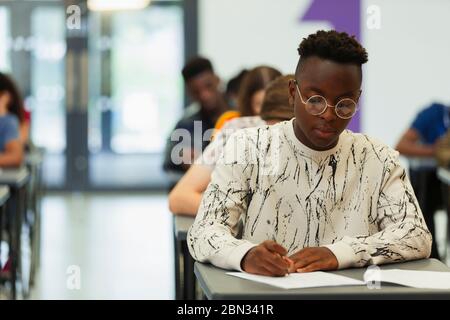 Teenage boy in eyeglasses sitting at desk and listening to lecturer ...