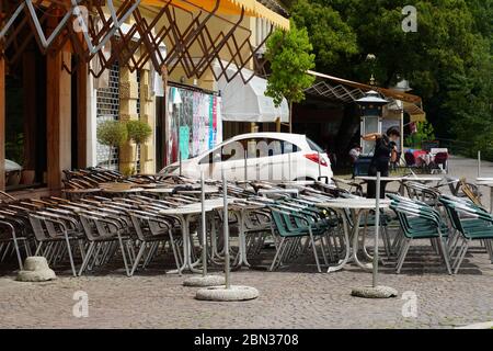 Italian restaurants in Merano, South Tyrol, are still closed because of COVID-19. Chairs and tables stacked up and chained together. Lady cleaning Stock Photo