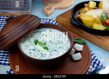 Okroshka - summer cold soup. Cold soup with fresh cucumbers, radishes, potato and sausage. Traditional russian food. Okroshka with kefir and rosemary Stock Photo