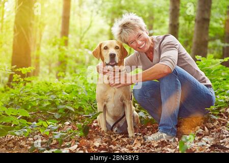 Elderly smiling woman sits with dog in forest Stock Photo