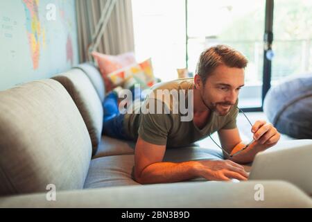 Man relaxing, laying on sofa using laptop Stock Photo