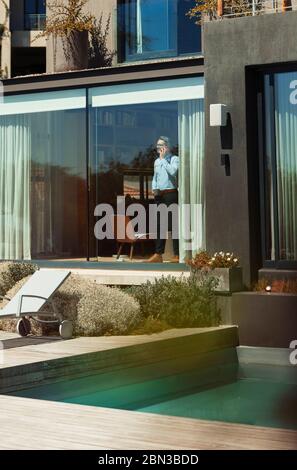 Businessman talking on smart phone at sunny, luxury patio window Stock Photo