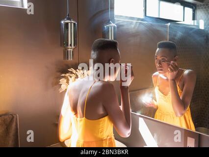 Young woman applying mascara in sunny bathroom mirror Stock Photo
