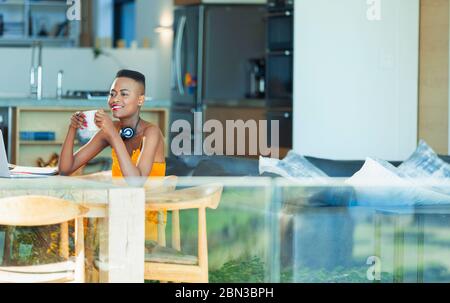 Smiling young woman drinking coffee at dining table Stock Photo