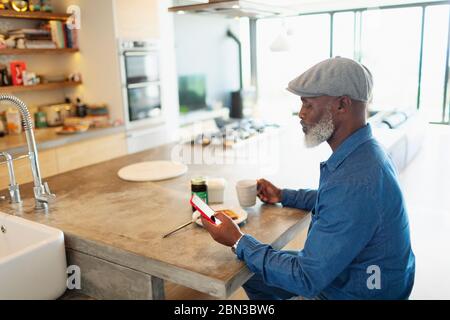 Man enjoying breakfast and using smart phone in morning kitchen Stock Photo
