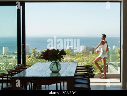 Young woman standing on modern balcony with sunny ocean view Stock Photo