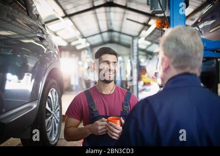 Smiling, happy male mechanics talking and drinking coffee in auto repair shop Stock Photo