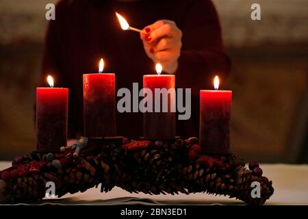 Advent wreath with red candles. Woman lights fourth candle.  France. Stock Photo