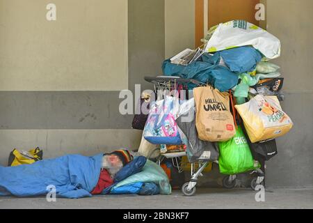 Munich. 12th May, 2020. Public life in times of the coronavirus pandemic on May 12, 2020 in Munich. A homeless man, bum sleeps on the ground in the courtyard arcades, arcades, courtyard garden. His belongings and possessions are packed in plastic bags and let a shopping cart overflow. He lies asleep wrapped in a quilt on the hard ground. | usage worldwide Credit: dpa/Alamy Live News Stock Photo