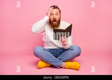 Full size photo astonished guy sit floor legs crossed read paper book impressed unexpected scream touch hand forehead wear jumper sweater bright Stock Photo