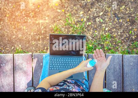 Woman using alcohol nano mist sprayer cleaning her hand before work with laptop to prevent the virus and bacterias. Quarantine for coronavirus (Covid- Stock Photo