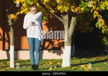 A young woman is frowning at her smartphone while texting. She is rubbing her shoulder in hopes of soothing her neck pain. Smartphone slump. Stock Photo