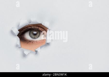 Female eye looking through torn paper Stock Photo