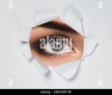 Female eye looking through torn paper Stock Photo
