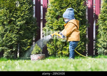 Small boy with watering can watering trees on backyard. Happy childhood concept Stock Photo