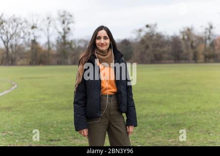 Casually dressed young Indian woman listening to earphones smiling in public park. Stock Photo